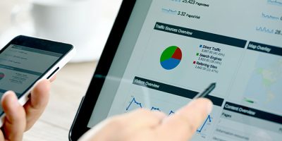 Charts and analytical data on the tablet screen with a cup of coffee and a telephone.